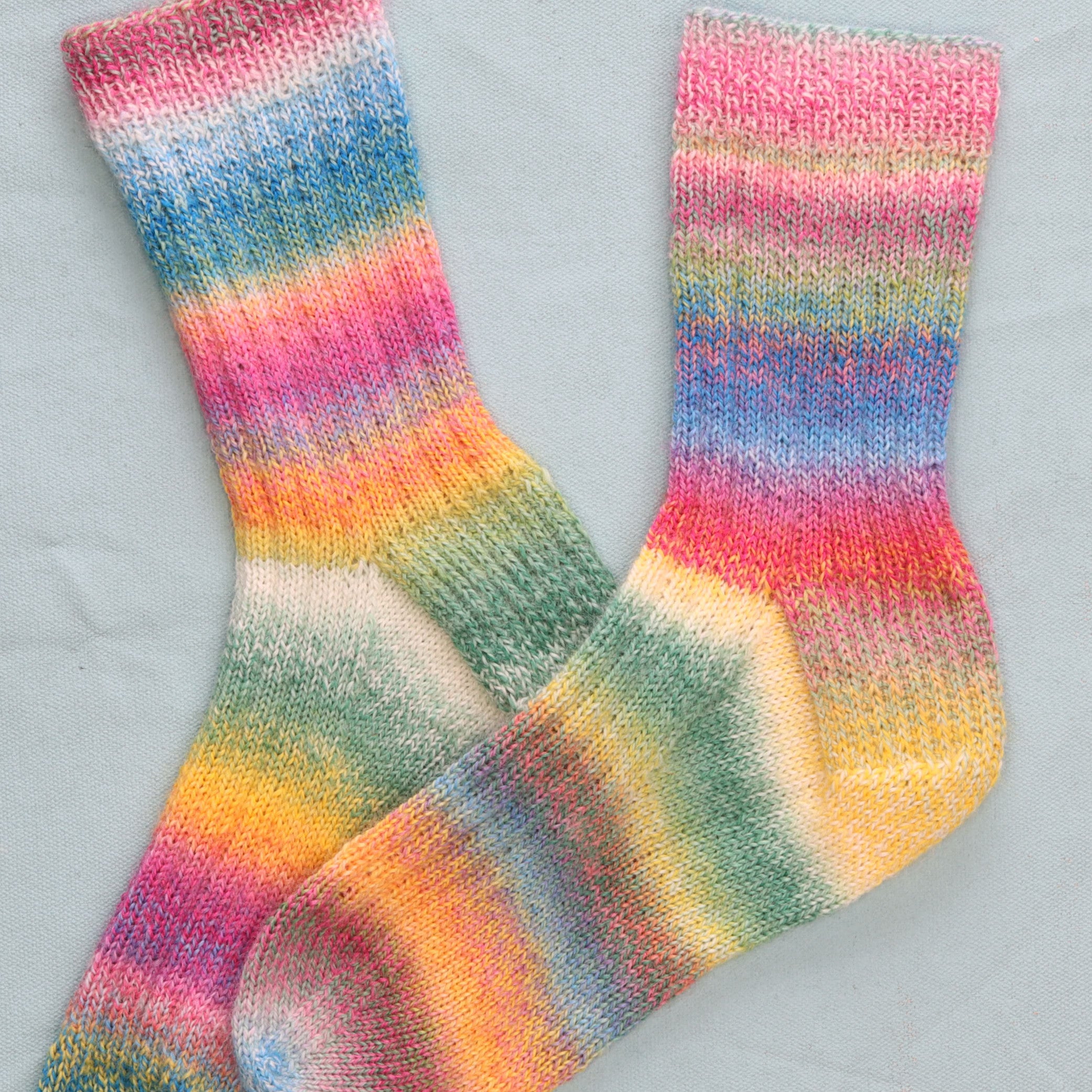 A pair of rainbow-striped hand-knitted socks laid flat to show both heels