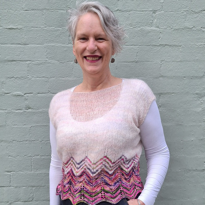 Woman wearing a white long-sleeve shirt with a colorful zigzag patterned vest against a gray brick wall.