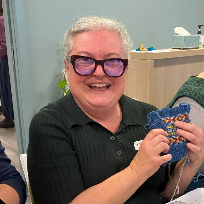 Woman wearing glasses holding a knitted item in an indoor setting
