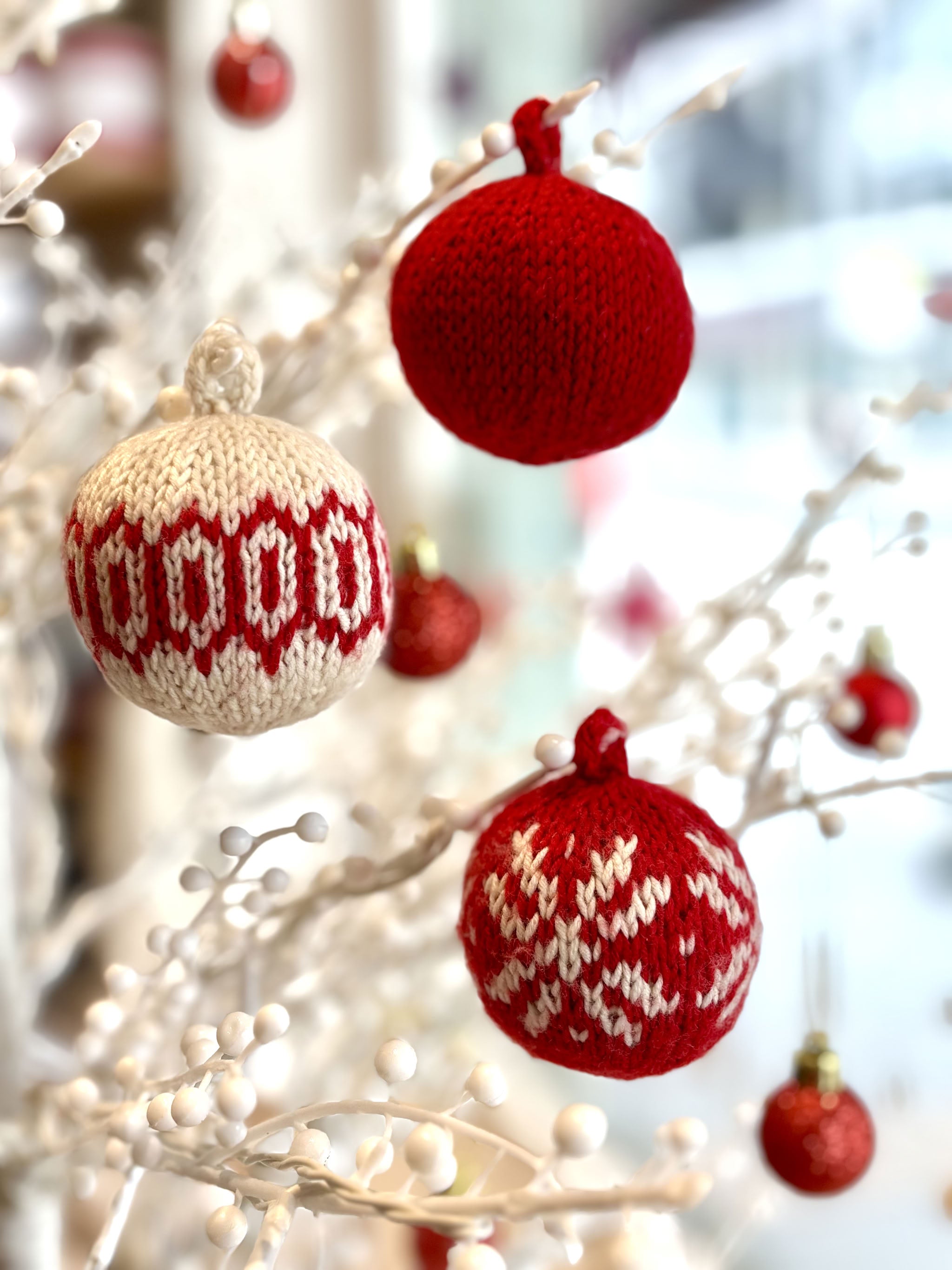 Three hand-knitted Fair Isle Christmas baubles in red and cream hanging on a white twig tree