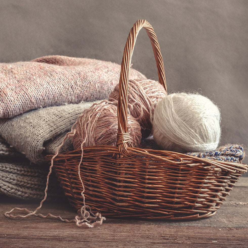 Wicker basket of yarn balls in front of folded knitted jumpers