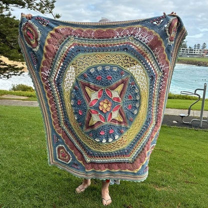 Universe in Bloom Blanket crochet kit – finished blanket in Gum Blossom held up by the sea