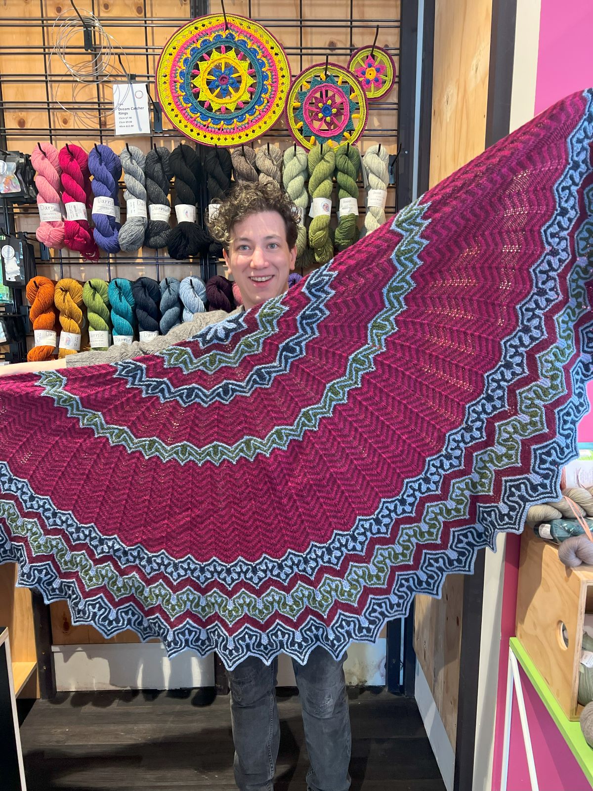 Xandy Peters holding up a colourful knitted shawl at Skein Sisters